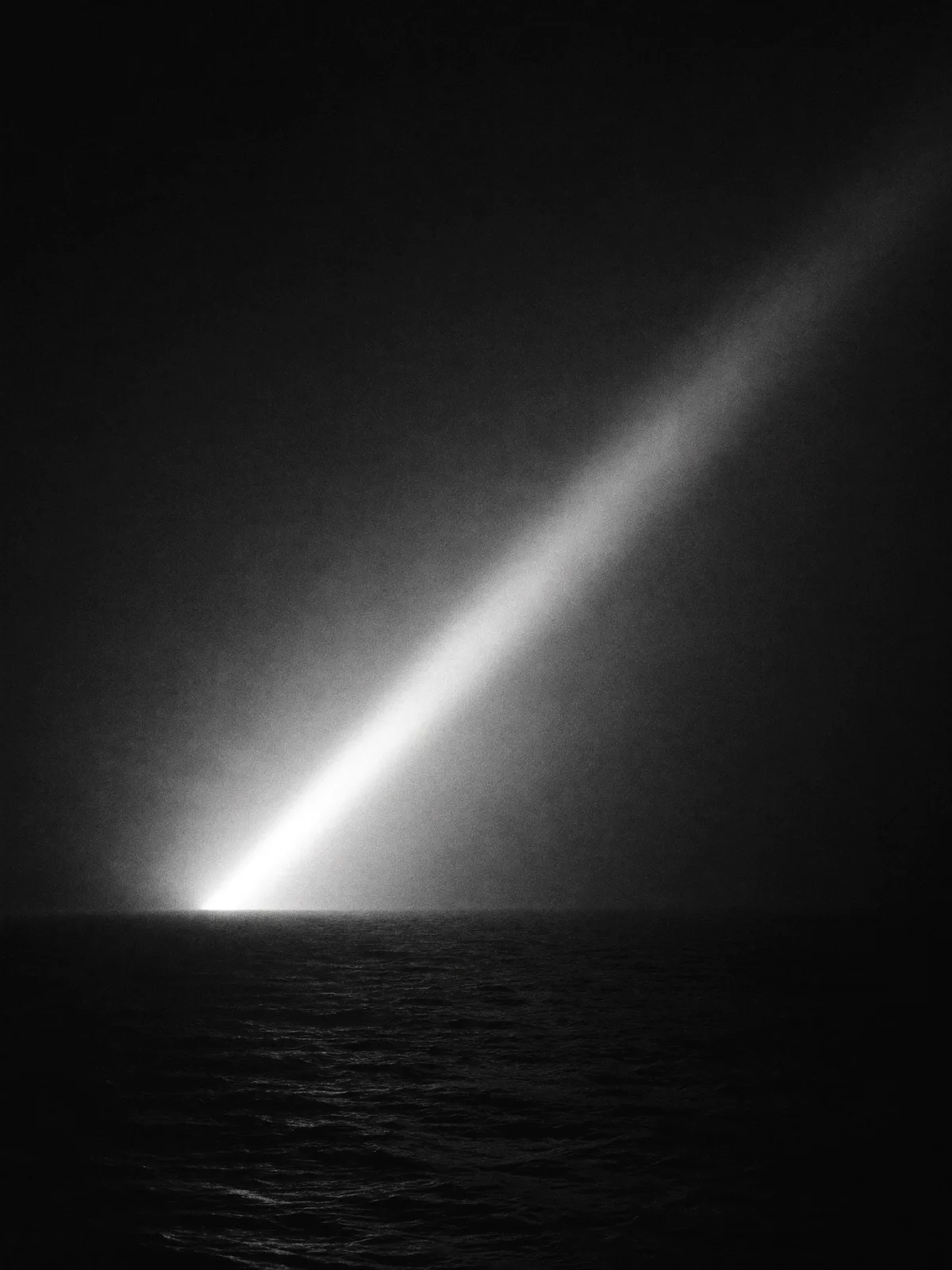 Faisceau de phare balayant la brume au-dessus d'une mer sombre, noir et blanc